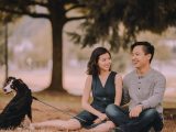 Glad ethnic couple with Bernese Mountain Dog on leash sitting on grass while spending time together on weekend